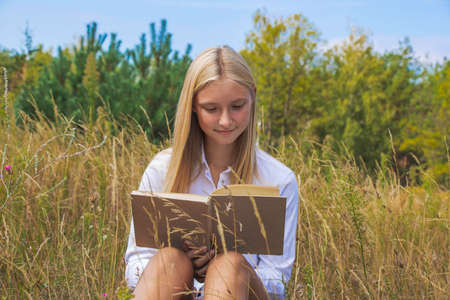 Beautiful girl reads a book on nature guy wants to give a bouquet of flowers in summer and fallの写真素材
