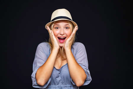 A beautiful girl in a hat, expresses emotions of joy and admiration, close-up on a dark background.の写真素材