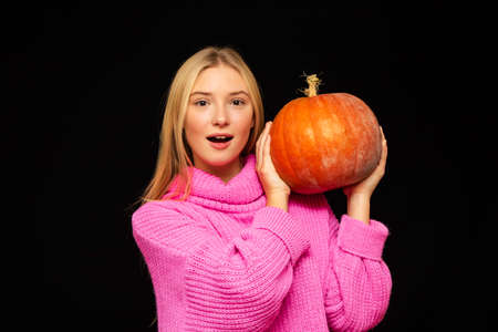 cheerful girl holding a large pumpkin in her hands close-up on a dark backgroundの写真素材
