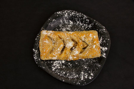 Sweet delicious pie sprinkled with powdered sugar on a black diet plateの写真素材