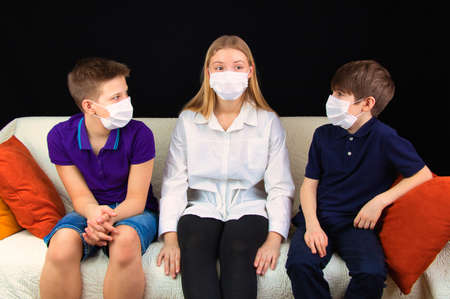 Children in medical masks sitting on the couch discussing a school assignment, close-up,の写真素材
