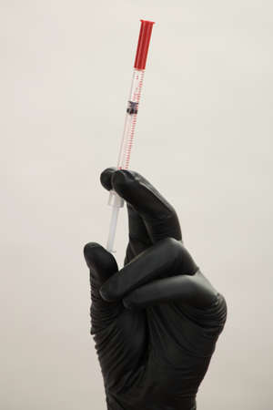 A hand in a black glove holds an injection syringeの写真素材
