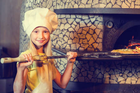 A baker girl in uniform serves pizza in the kitchen fireplace.の写真素材