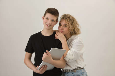 A boy with a charming smile stands next to his mother and holds a laptop in his hands. White background.の写真素材