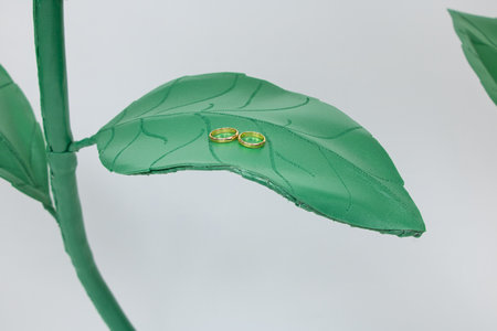 Golden wedding rings lie on a green leaf of artificial roses.の写真素材