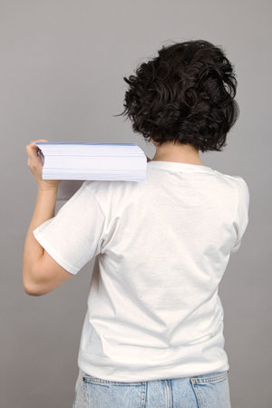 Woman with a stack of white paper on her shoulder, turned her back, close-up on a gray background.の写真素材