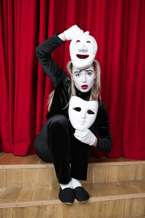 Portrait of a mime girl with masks in her hands, sitting on a theater stage.の写真素材