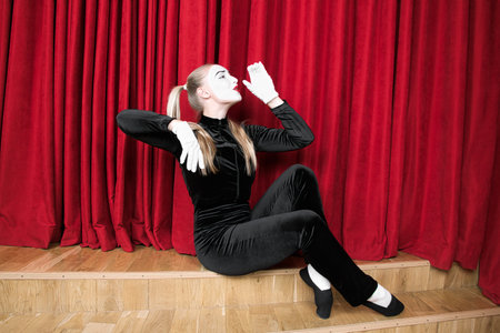 Pantomime, actress with an invisible glass in her hand, against a red curtain.の写真素材