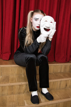 The focus is on a mime artist with a mask in his hand.