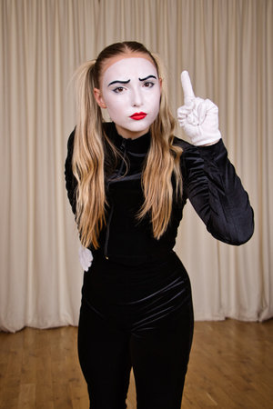 Portrait of a female mime in a black dress and white gloves showing a sign of attention, close-up.の写真素材