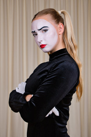 Close-up portrait of a mime girl in a black dress and white gloves, with a sad look.の写真素材