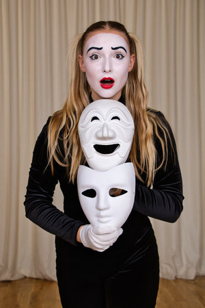 Portrait of a surprised mime girl with masks in her hands, close-up.の写真素材