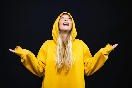 Portrait of a young woman in yellow hoodie on black backgroundの写真素材