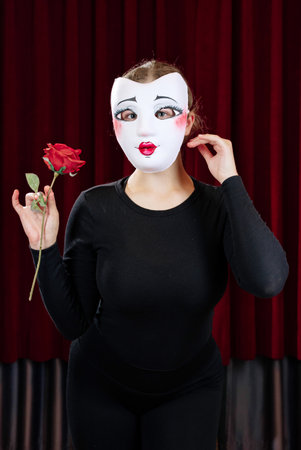 A mime girl with a red rose against a red curtain. Close-up.の写真素材