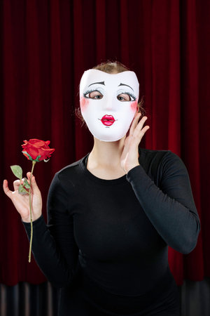 A mime girl with a red rose against a red curtain. Close-up.の写真素材