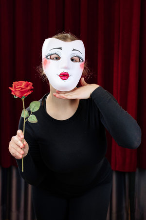 A mime girl with a red rose against a red curtain. Close-up.の写真素材