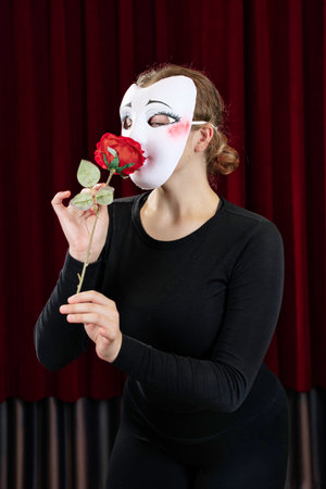 A mime girl with a red rose against a red curtain. Close-up.の写真素材