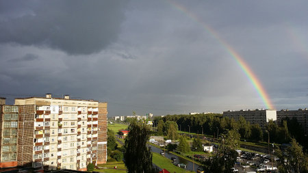 A vibrant rainbow shines above the urban landscape of Riga, Latvia, right after the summer rain. The sunlight and storm clouds create a dramatic contrast over the city buildings.の写真素材