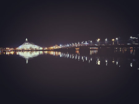 Night cityscape of Riga, Latvia, with reflections of lights and architecture on the calm Daugava River in winter.の写真素材