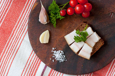 Sandwich made of salted lard on rye bread, served with garlic, cherry tomatoes and parsley