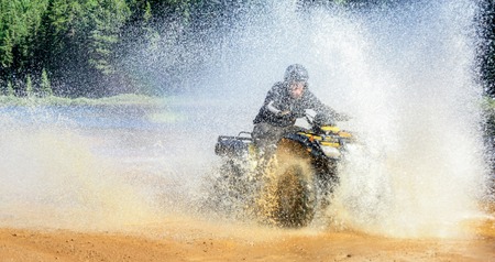 Man driving ATV quad through splashing water with high speed.の写真素材