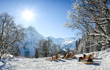 Group of people sitting with deck chairs in winter mountains. Sunbathing in snow. Germany, Bavaria, Allgau, Schwarzenberghuette.の写真素材