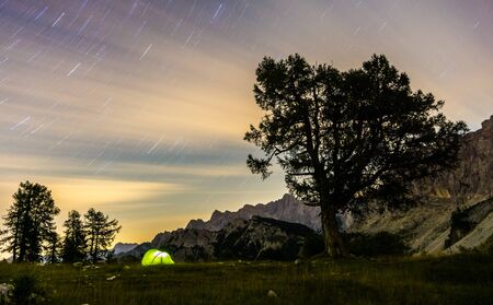 Illuminated camping tent at night. High altitude alpine landscape. Shining Stars in dark blue sky with purple clouds. Triglav National Park, Mountain Slemenova, Sleme, Slovenia.の写真素材