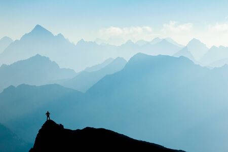 Man reaching summit after climbing and hiking enjoying freedom and looking towards mountains silhouettes panorama in early Morning.の写真素材