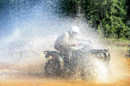 Man driving motocross ATV quad through splashing river lake water with high speed. Foy, Foyross Lake, Sudbury, Canada.の写真素材