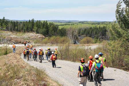 SUDBURY, ONTARIO, CANADA - MAY 21 2009: Group of workers and geologists in hardhats and high visible vests inspecting site. View from the back. Walking on dirt road to rock formation.のeditorial素材