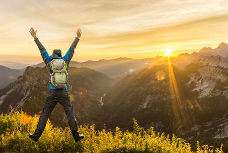 Hiking Man with Backpack jumping with raised arms on mountain. Amazing sunrise Backlight with beautiful lens flares and sunbeams. Julian Alps, Triglav National Park, Slovenia, Slemenova, Sleme.の写真素材