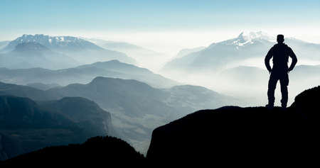 Spectacular layered mountain ranges with valley fog. Man Silhouette reaching summit enjoying...