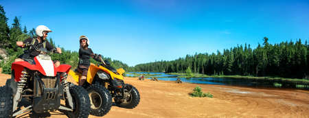 Quad ATV driving people. Happy smiling couple bikers on beach at beautiful lake. Foy, Foyross Lake,...