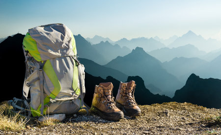 Hiking equipment with blue mountain silhouettes. Backpack and boots on top of mountain. Tyrol, Austria.の写真素材