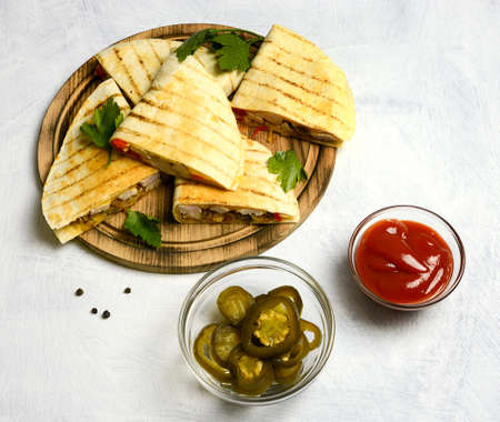 Quesadillas on a wooden plate on a white background. Red sauce. and jalapeno pepper Top view