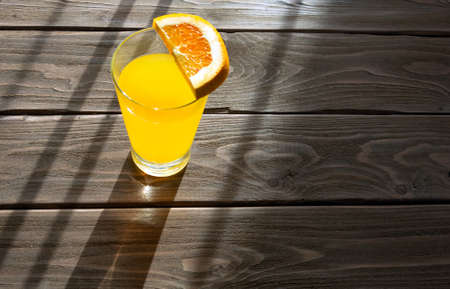 Orange drink in a glass cup with an orange slice on a wooden table.の写真素材