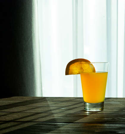 Orange drink in a glass cup with an orange slice on a wooden table.
