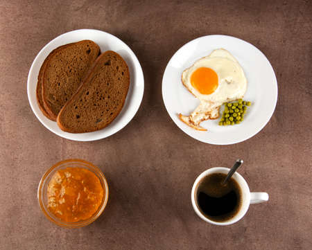 Classic breakfast: fried eggs, jam, bread, coffee in a white cup on a dark background.