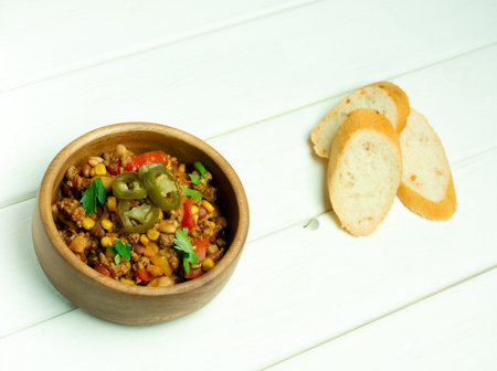 Bowl with chili con carne, white wooden background, slices of white breadの写真素材