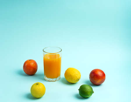 A glass of orange juice surrounded by limes, lemons and oranges on a blue background. Copy space.の写真素材