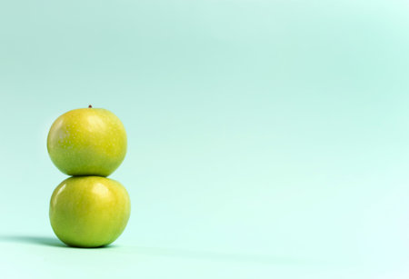 Two green apples standing on top of each other on a blue background. Copy space. Horizontal orientation. High quality photoの写真素材