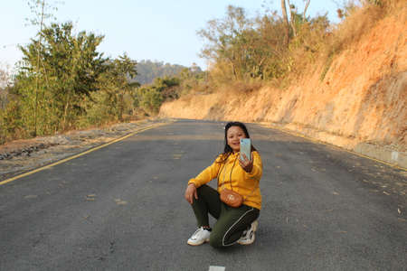 teen girl sitting in the middle of road and showing her smartphone , the latest technology related modern fashionの写真素材