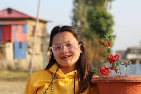 A Beautiful girl is wearing eyeglass with yellow color hoodie near flower on blur background as a...