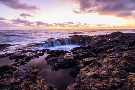 Sunset at El Bufadero natural blowhole on Gran Canaria. Ocean waves hitting rocks. Long time, Yellow blue sky. Some clouds.の写真素材