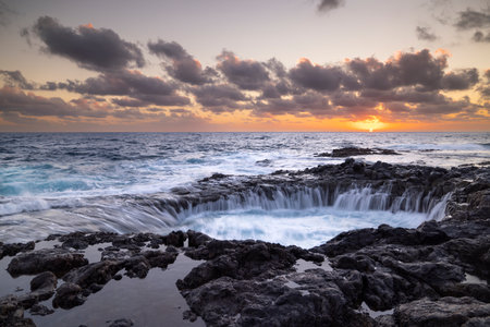 Sunset at El Bufadero natural blowhole on Gran Canaria. Ocean waves hitting rocks. Long time, Yellow blue sky. Some clouds.の写真素材