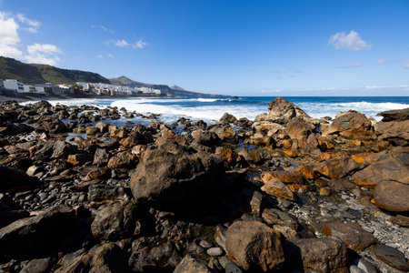 Coastal Charm: The Ocean Meets White Buildings and Rolling Hills in the Background. Waves hitting the rocks on the shore. Daylight, no clouds, no people.の写真素材