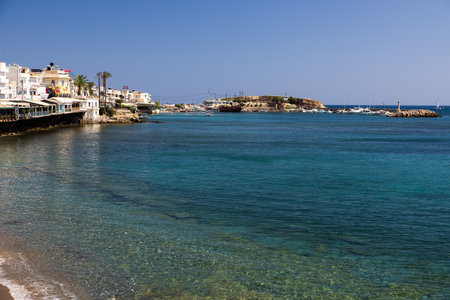 Bask in the sun's embrace as you gaze upon Hersonissos' vibrant shore and bustling port. On the left, quaint restaurants adorn the scene, while ships and boats grace the waters, a picturesque holiday moment.の写真素材