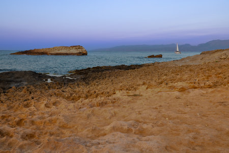 Witness the pure magic of daybreak along Crete's coastline as the sun begins its ascent. A rocky shoreline stands strong in the foreground, while two rocky islets emerge from the tranquil sea. The sky, painted in soft pink hues, signals the arrival of a new day over the serene Mediterranean waters, filling the moment with hope and wonderの素材 [FY310212316994]