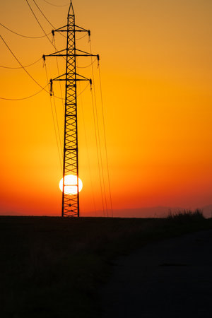 As the sun makes its ascent in the vast, cloudless sky, it paints a tranquil morning scene. The sun's radiant disk rises just behind a towering power pole, creating a striking silhouette. On the horizon, the contours of grasses and shrubs come into view, while the world awakens to the promise of a new day filled with possibilities and the warmth of the rising sunの写真素材