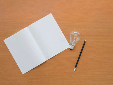 top view of notebook, light bulb and pencil on wooden table with copy spaceの写真素材
